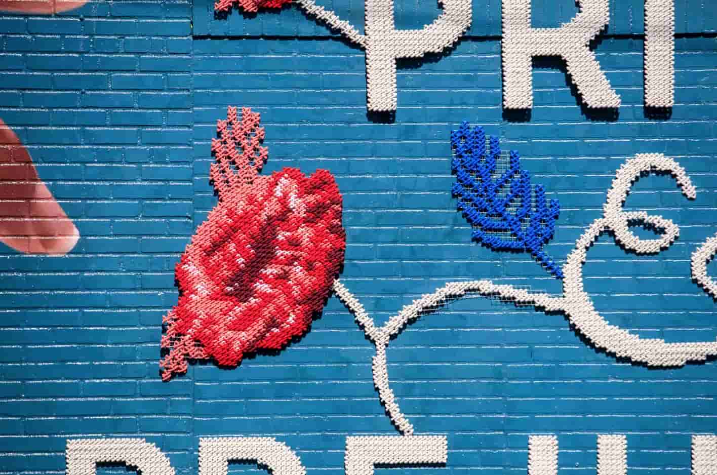 Audible Pride & Prejudice — close-up of red and blue embroidered flowers on brick wall