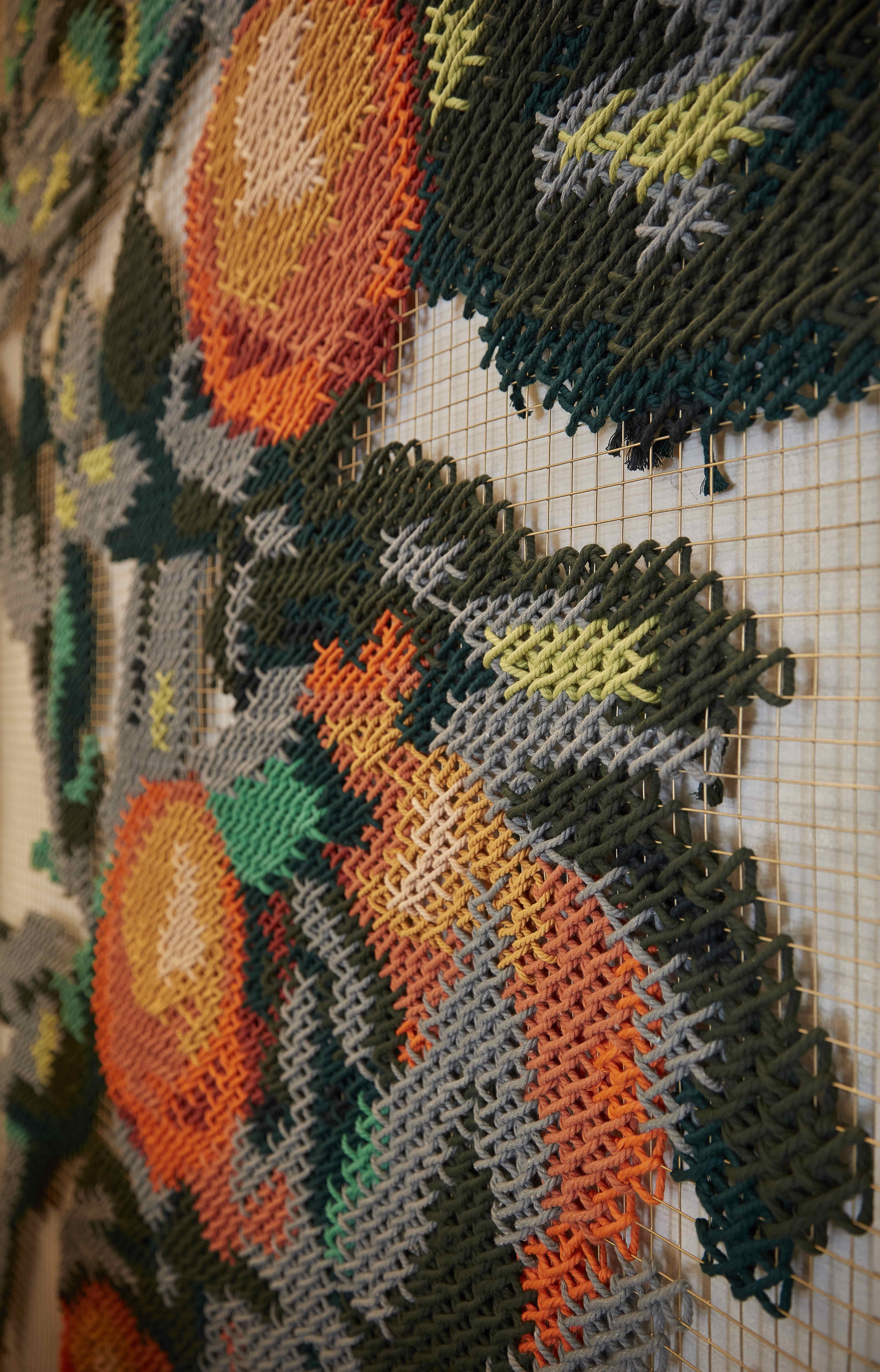Vaqueta — macro detail of orange embroidery stitch on metallic mesh